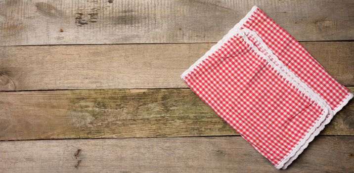 folded red and white cotton kitchen napkin on a wooden gray background, top view