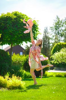 A charming girl in a light summer sundress and a pareo hat is walking in a green park. Enjoys warm sunny summer days.