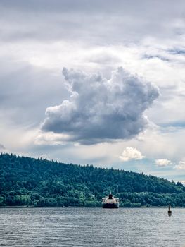Ocean-going freight vessel in Pacific ocean bay on mountain and cloudy sky background