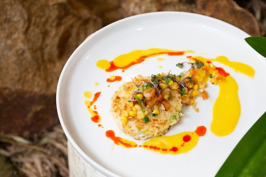 Gourmet crab cakes with dressing and vegetable slices.