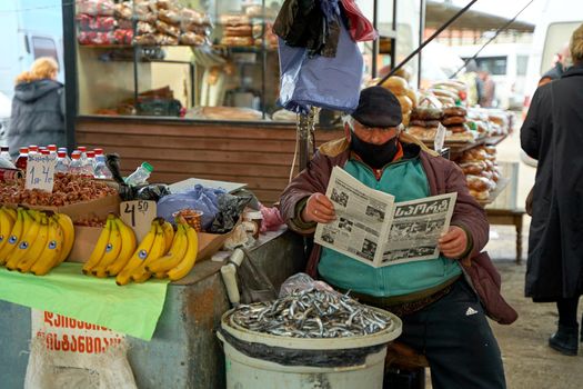 Overweight Georgian man. A street market seller reads a newspaper while sitting at the counter.