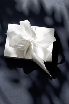 Anniversary celebration, shop sale promotion and luxe surprise concept - Luxury holiday white gift box with silk ribbon and bow on black background, luxe wedding or birthday present