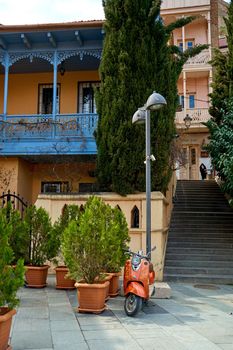The architecture of the old district of Tbilisi. A retro moped is parked in front of a stylish old building.