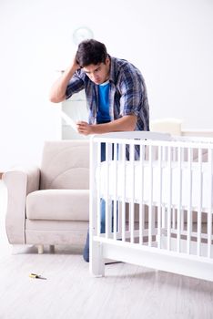 Young man assembling baby bed with instruction manual