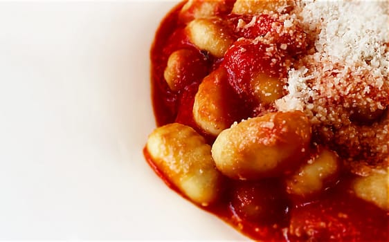 Close up of a portion of gnocchi in tomato sauce with grated parmesan cheese served in a white ceramic plate. Italian food and cuisine.