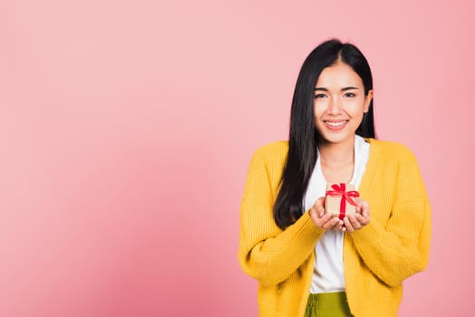 Portrait of happy beautiful Asian young woman smiling holding small gift box on hands, studio shot isolated on pink background, Birthday, New year, Christmas, valentine, holiday day concept