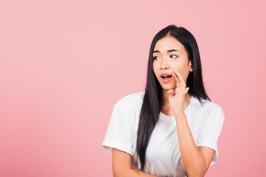 Asian happy portrait beautiful cute young woman teen standing hand on mouth talking whisper secret rumor studio shot isolated on pink background, Thai female looking to side away with copy space