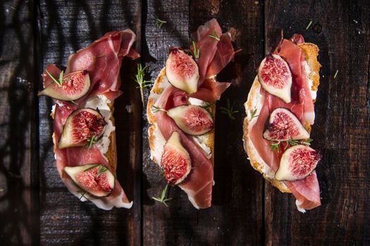 Presentation on wooden table bruschetta with figs and prosciutto