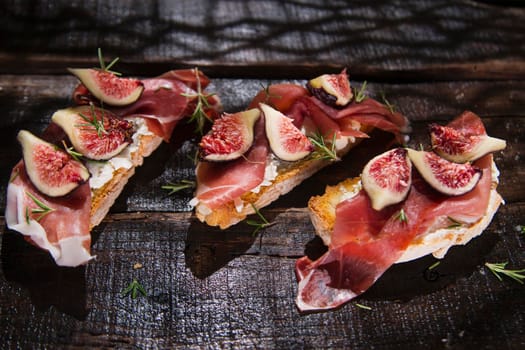 Presentation on wooden table bruschetta with figs and prosciutto