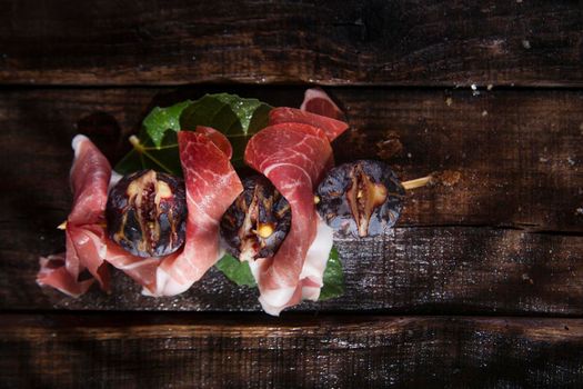 Presentation of skewers with prosciutto and figs blacks