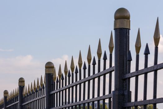 black iron fence with golden decorative elements in linear perspective with selective focus.