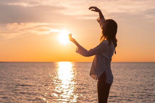 Silhouette of young happy carefree woman posing on the beach at sunset