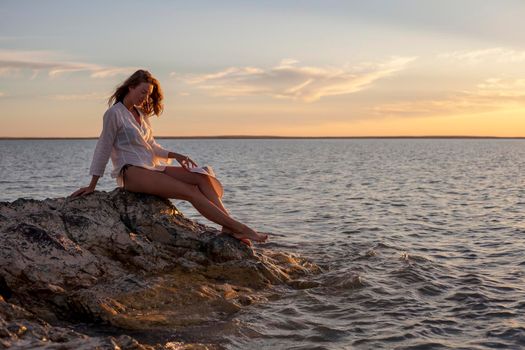 Beautiful woman enjoying sunset on the beach, sitting on rocks