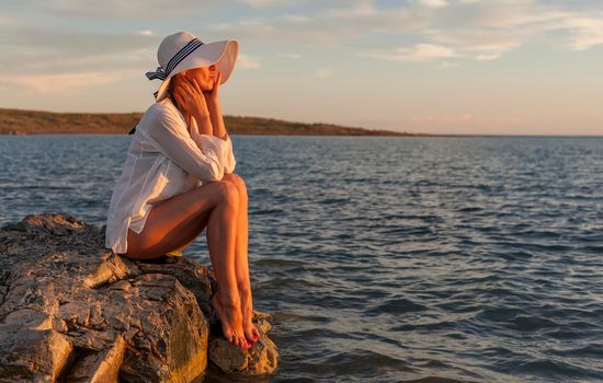 Beautiful woman enjoying sunset on the beach, sitting on rocks