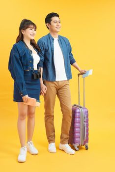 Happy excited young Asian couple tourists in colorful yellow background