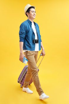 Stylish male tourist in hat carrying suitcase isolated on yellow, travel concept