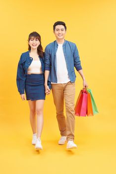 Asian couple shopping, full length portrait isolated on yellow background.