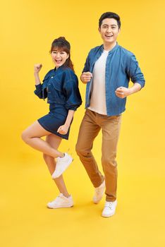 Portrait of funky couple jumping in air holding hands up enjoying time together isolated on yellow background