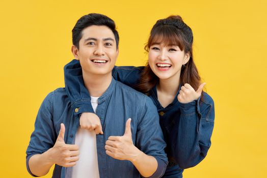 Attractive smiling young Asian couple being happy and amazed isolated on yellow studio background