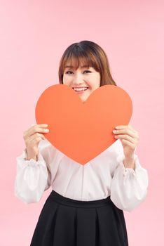 Cute asian woman holding red heart isolated on pink