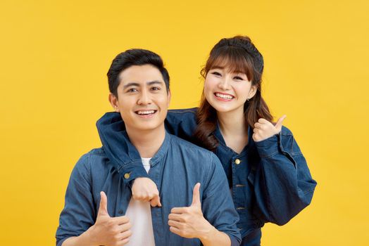 Image of joyous couple showing thumbs up while man piggybacking joyful woman isolated over yellow background