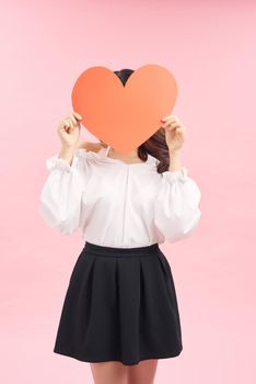 Beautiful asian girl with a card in the shape of a heart in her hands on a pink background.
