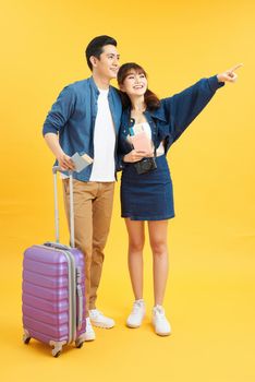 Portrait of a young beautiful couple with suitcase and looking up. Travel concept. Isolated yellow background.