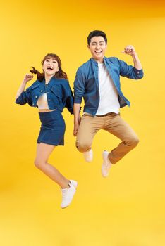 Full length portrait of amazed couple man and woman in basic t-shirts rejoicing while clenching fists isolated over yellow background