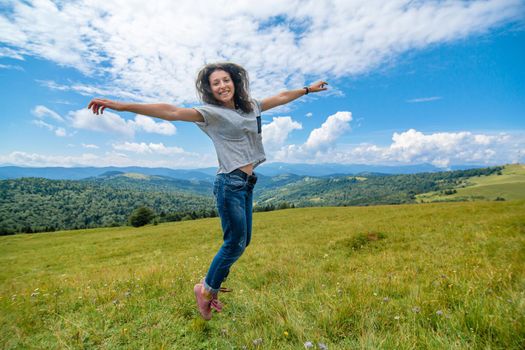 Happy gorgeous girl enjoy mountain view jumping on the hill with breathtaking mountain landscape.