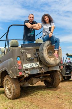 Happy young couple resting on the dirty offroad car. Highland car tour.