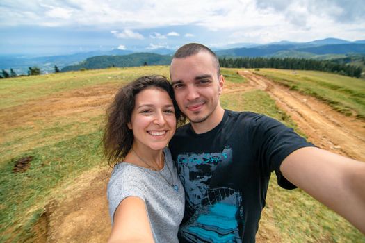Young couple hugs and take selfie with amazing mountain landscape background.