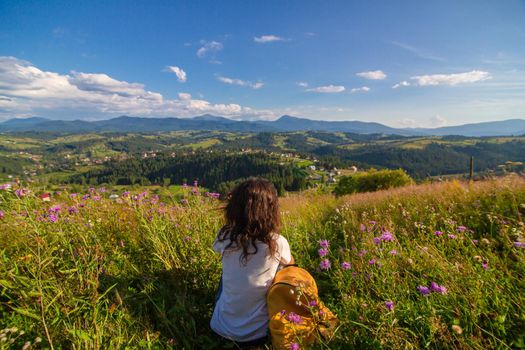Happy gorgeous girl enjoy hills view sitting in flower field on the hill with breathtaking nature landscape.