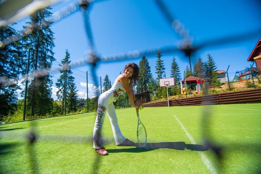 Slim gorgeous girl ready to play in tennis on court in bright summer day.