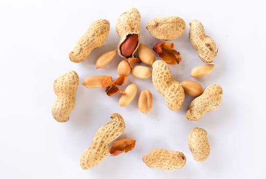 Peanuts are scattered on a white background, some are removed to reveal the red seeds inside.