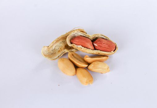 Peanuts piled up separately on a white background . One has been peeled off to reveal a red seed inside. There are two seeds that have been carved apart in front.