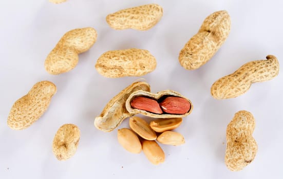 Peanuts scattered on a white background. One was opened to reveal a red seed inside.