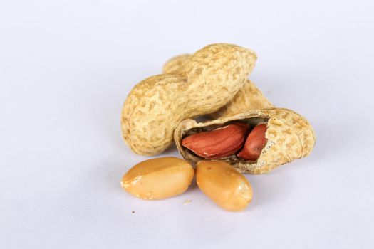 Peanuts isolated on white background . Two kernels are already unpacked. One of the peanuts, which was removed, revealed a red seed on the side.