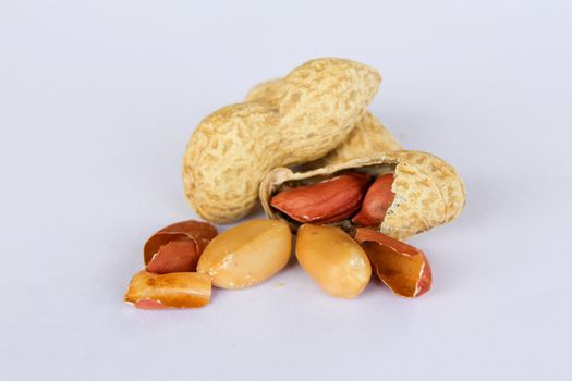 Peanuts isolated on white background . Two kernels are already unpacked. One of the peanuts unpacked reveals a red seed on the side. On the sides there is a peeled seed coat.