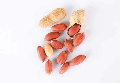Red and peeled peanuts on a white background. One peanut was peeled, revealing a red seed inside.