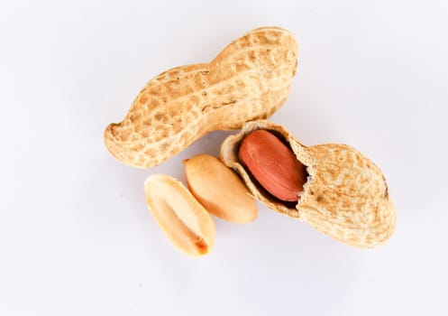 Top view of peanuts on a white background. Peanuts are shelled to reveal red seeds inside. There was a seed that had been removed on the side.