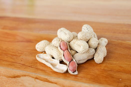Peanuts on a wooden table. One peanut was peeled to reveal the red seed inside.