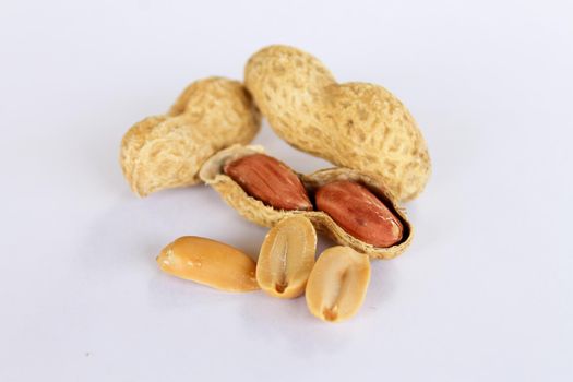 Peanuts isolated on white background . Two kernels are already unpacked. One of the peanuts unpacked reveals a red seed on the side. The seeds are separated from each other in the front.