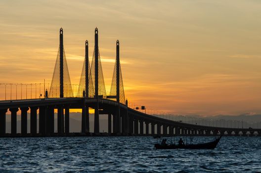 Silhouette fishing boat near Penang Second Bridge during sunrise.