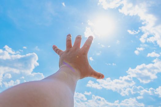 Man pulls his hand to the sun against the background of the sky in the clouds