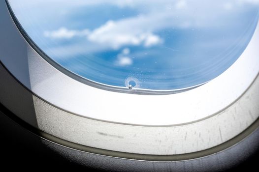 Tiny hole or bleed hole in airplane window compensate for difference between the pressure inside the cabin of a plane and that outside of the plane.