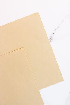 Beige A4 papers on white marble background as office stationery flatlay, luxury branding flat lay and brand identity design for mockups