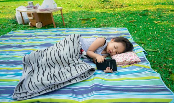 little girl looking at mobile phone while lying in the park
