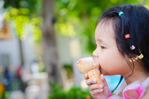 Asian little girl eating an ice cream outdoors with natural light blur background