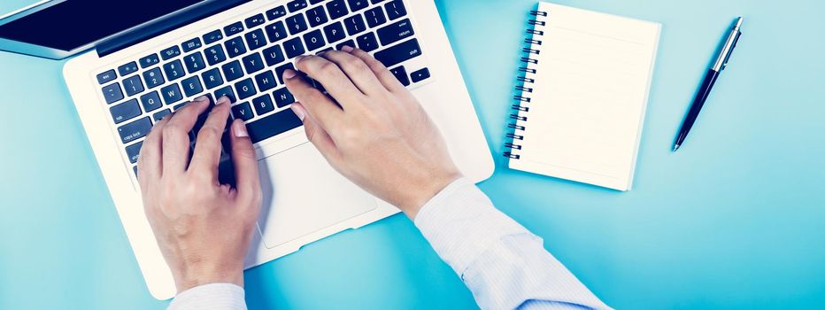 Flat lay, hand of businessman working on laptop computer with cup of coffee on desk in office, workplace and notebook and book on blue background, workspace and copy space, top view, business concept.