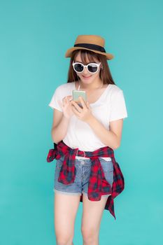 Beautiful portrait young asian woman listening music on phone with earphone isolated on blue background, asia girl using smartphone excited and fun with relax in travel summer trip concept.